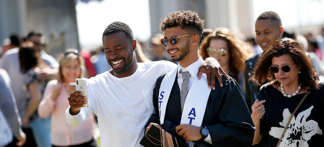 Two smiling Black men, one a graduate, take a selfie after commencement